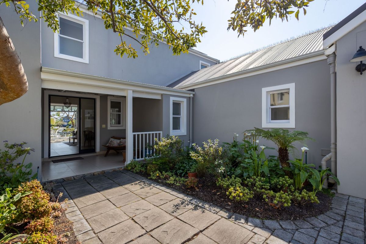 A well-maintained rear exterior featuring a paved patio area, landscaped garden beds, and a covered porch entrance with modern grey facade finishes.