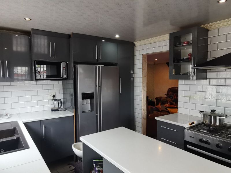 Modern kitchen featuring dark grey cabinetry, white subway tile backsplash, stone countertops, and integrated appliances including a gas stove and built-in microwave.