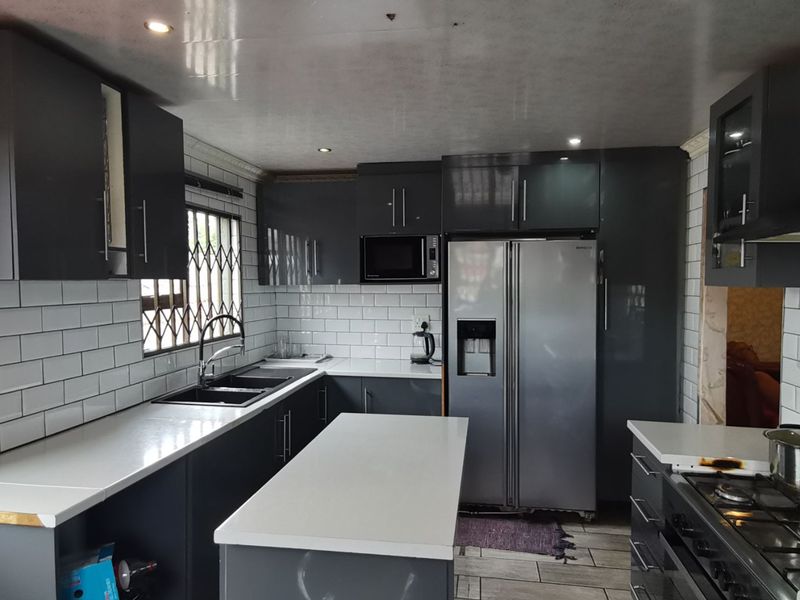 Modern kitchen featuring dark grey cabinetry, white quartz countertops, subway tile backsplash, and integrated appliances with recessed lighting.