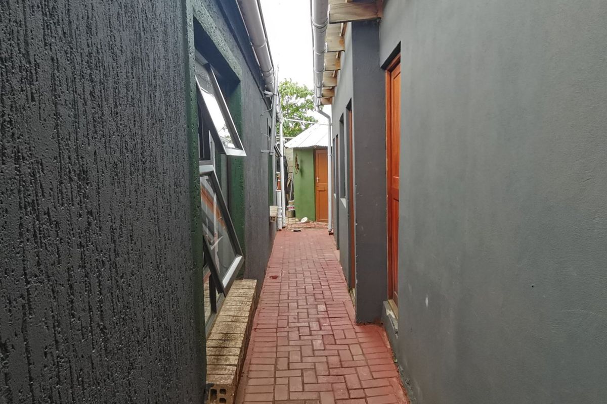 A narrow exterior side passage featuring paved brick flooring, dark textured wall finishes, and access points to the property.