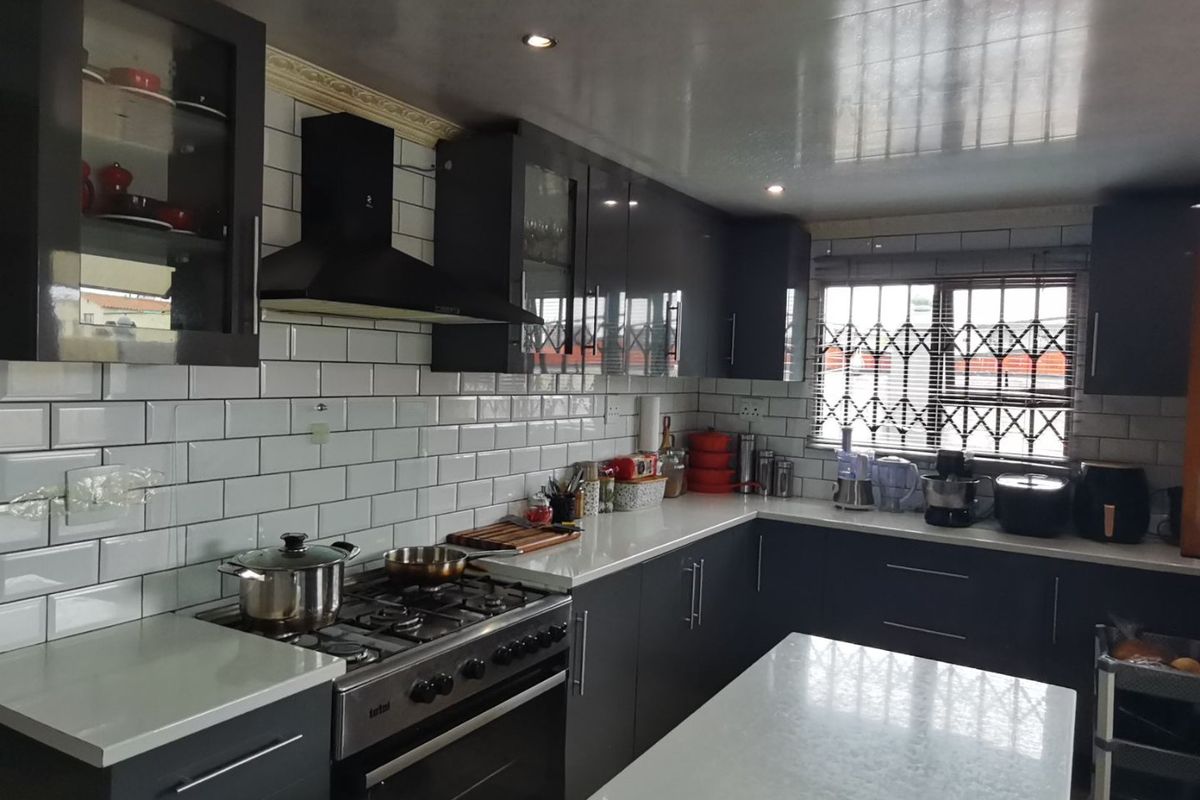 Modern kitchen featuring dark cabinetry, white quartz countertops, subway tile backsplash, and a gas stove with an integrated extractor fan.