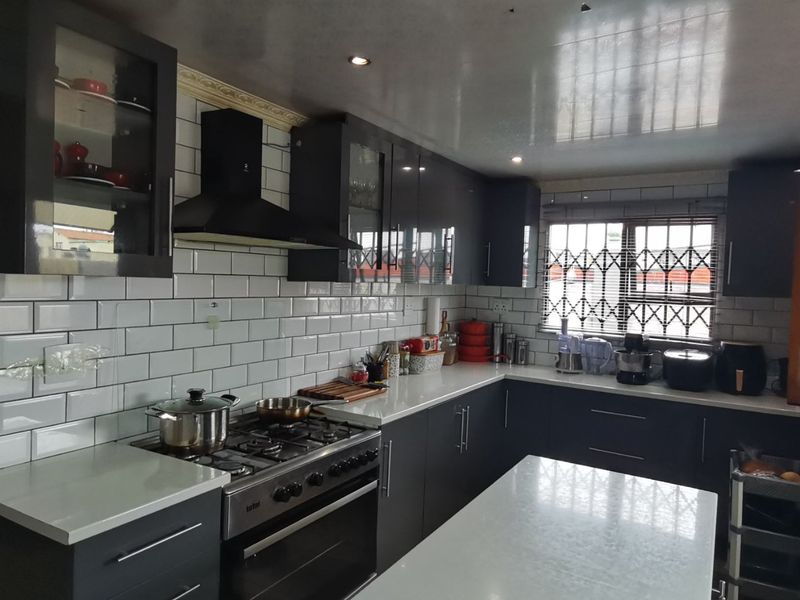 Modern kitchen featuring dark cabinetry, white quartz countertops, subway tile backsplash, and a gas stove with an integrated extractor fan.