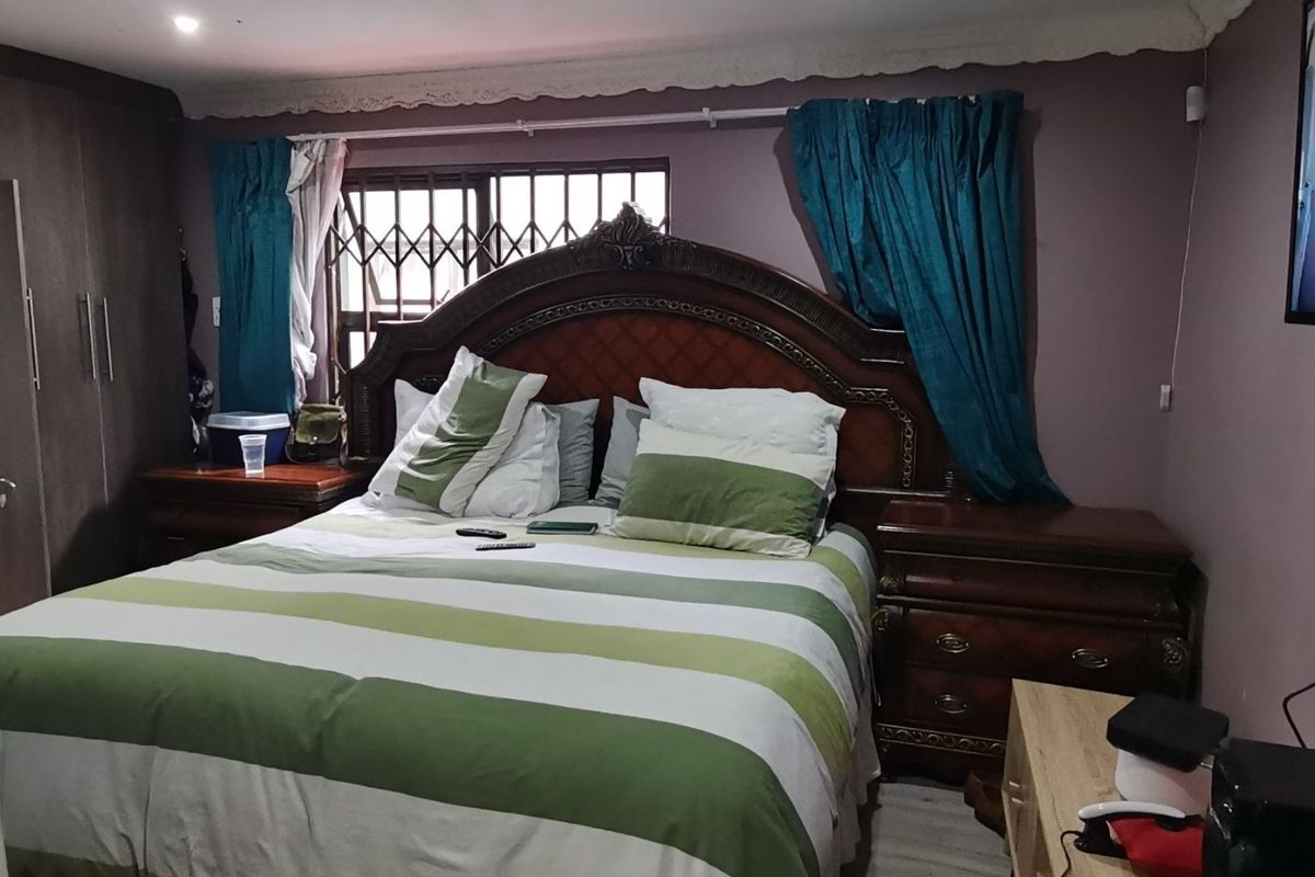 A bedroom featuring built-in cupboards, laminate flooring, and recessed downlights, with a security gate installed on the window.