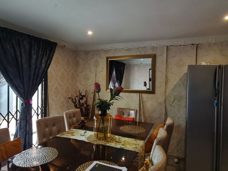 Dining room featuring decorative cornice and patterned wallpaper, currently showing signs of wear with peeling wall coverings.