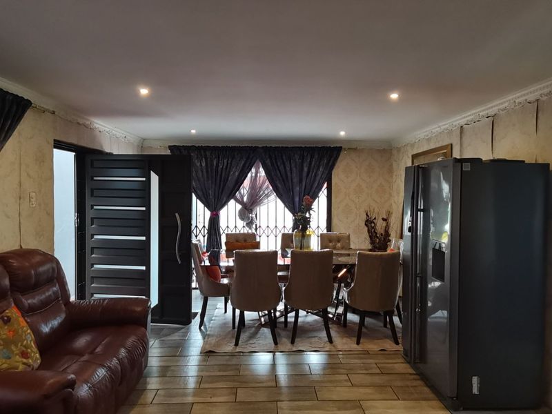 Open plan living and dining area featuring tiled flooring, recessed lighting, and decorative ceiling cornices, currently showing signs of wear on the wall finishes.