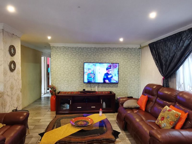 A living room featuring tiled floors, recessed downlighting, and a wallpapered feature wall, showing signs of wear and peeling finishes.