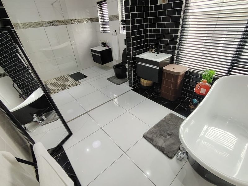 Modern bathroom featuring a freestanding bathtub, walk-in shower, wall-mounted vanity, and striking black and white tiled finishes.