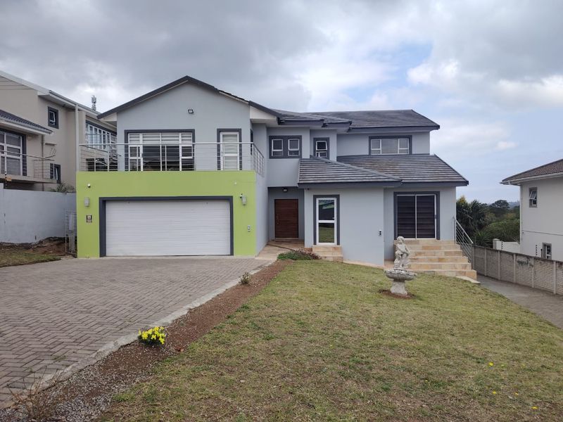 A modern two-story residential home featuring a double garage, upper-level balcony, paved driveway, and stone entrance steps.