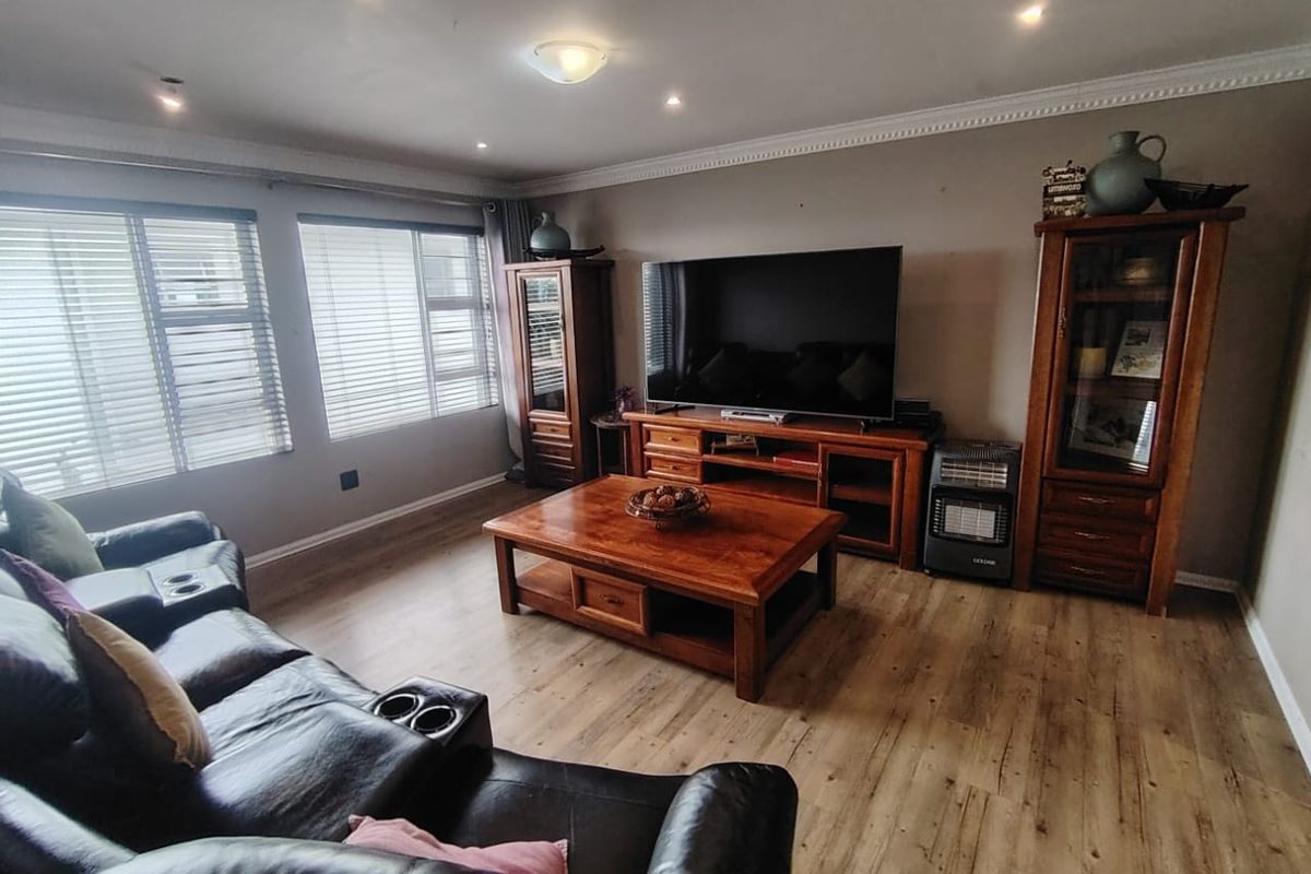 A comfortable living room featuring laminate flooring, recessed downlighting, and decorative ceiling cornicing, providing a functional and well-maintained space.