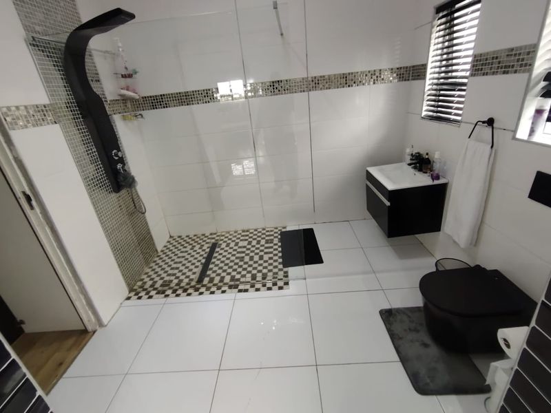 Modern bathroom featuring a walk-in shower with a sleek shower panel, wall-mounted vanity, and contemporary mosaic tile accents.