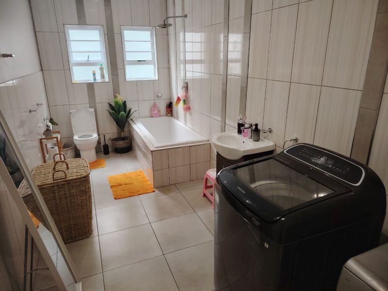 A functional bathroom featuring a built-in bathtub, shower, pedestal basin, and toilet, finished with neutral wall and floor tiling.