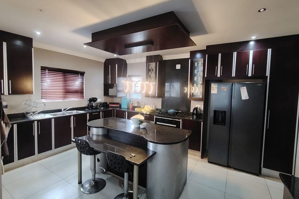Modern kitchen featuring dark wood cabinetry, granite countertops, a central island with breakfast bar, and integrated appliances under a stylish drop ceiling.