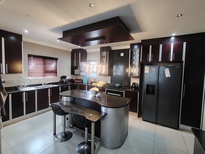 Modern kitchen featuring dark wood cabinetry, granite countertops, a central island with breakfast bar, and integrated appliances under a stylish drop ceiling.