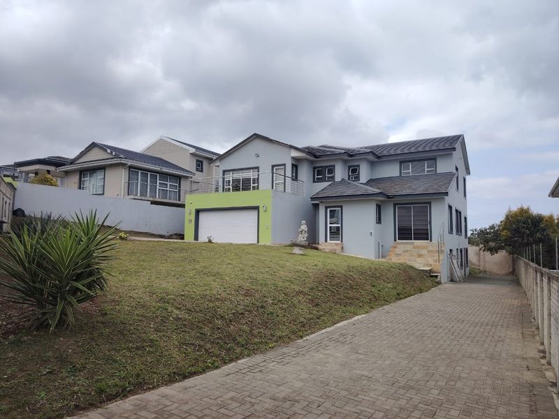 A modern double-story house featuring a paved driveway, double garage, and an upper-level balcony with stainless steel railings.