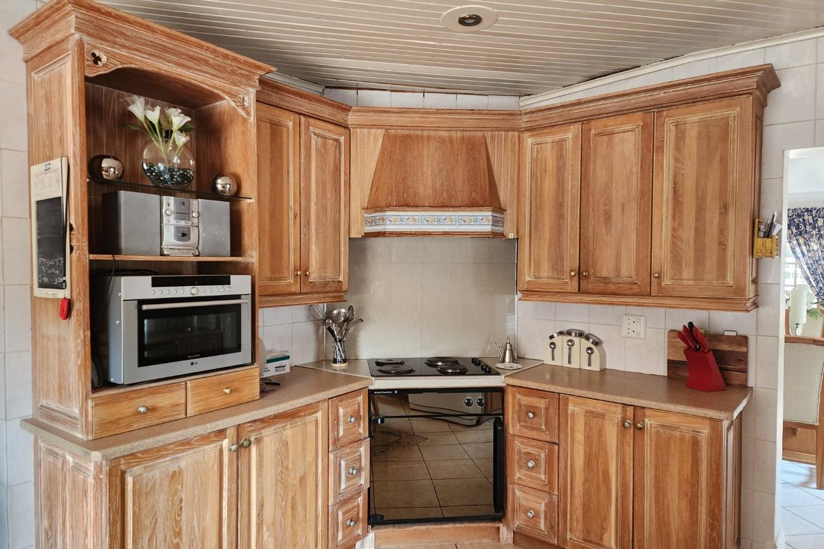A functional kitchen featuring traditional wooden cabinetry, a built-in oven with electric hob, and tiled finishes throughout.