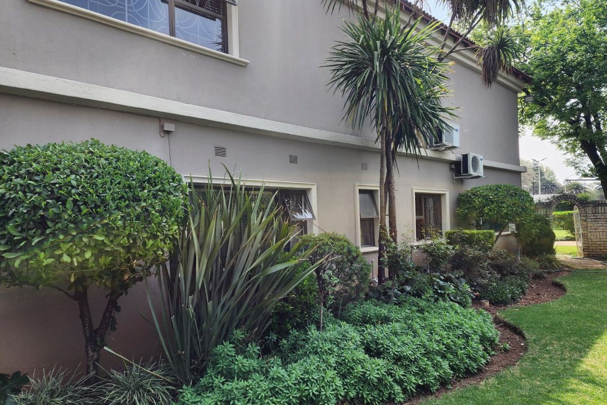 A view of the rear exterior elevation of the house featuring established garden landscaping and wall-mounted air conditioning units.