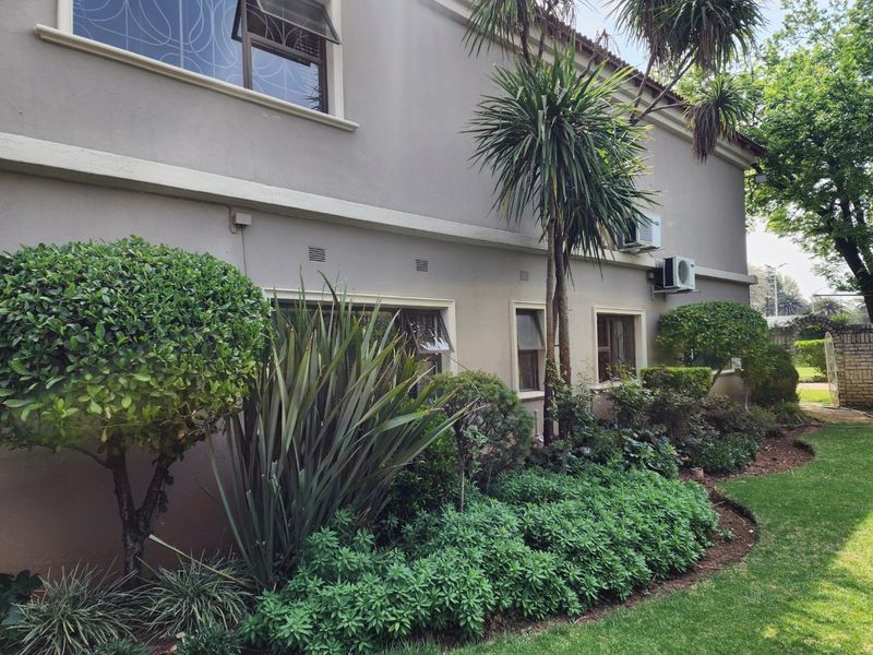 A view of the rear exterior elevation of the house featuring established garden landscaping and wall-mounted air conditioning units.