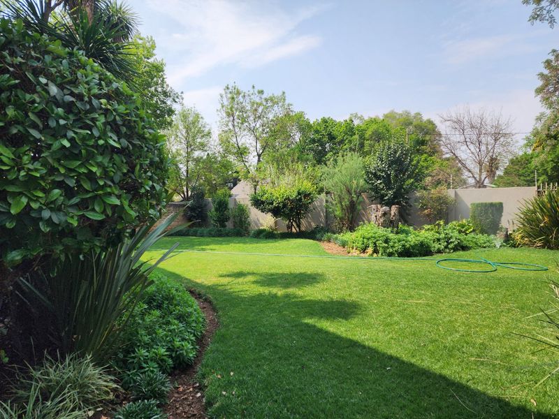 A well-maintained, spacious private garden featuring a lush green lawn, mature trees, and established garden beds enclosed by a perimeter wall.