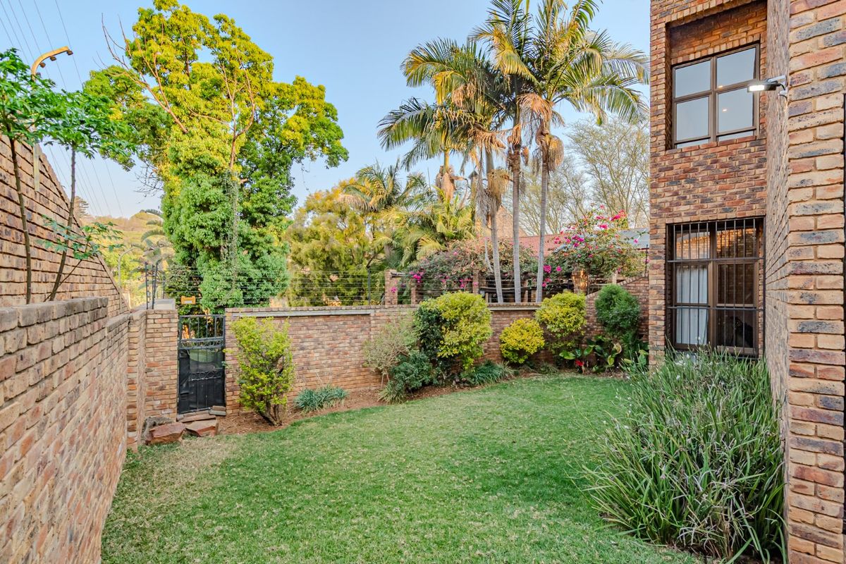 A private rear garden featuring a well-maintained lawn, face brick boundary walls, and established landscaping with security features.