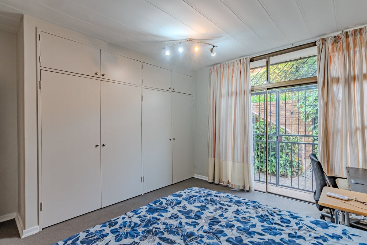 Bedroom featuring extensive floor-to-ceiling built-in cupboards, track lighting, and a sliding glass door providing direct access to an outdoor area with security gate.