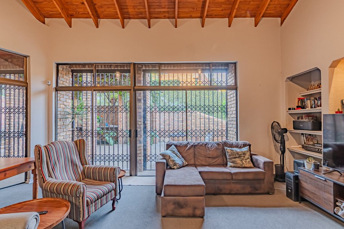 Spacious living room featuring a high exposed timber beam ceiling, large sliding glass doors with security gates, and built-in shelving.