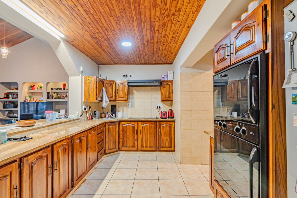 A functional kitchen featuring warm timber ceilings, granite countertops, and traditional wooden cabinetry with a built-in oven and tiled finishes.