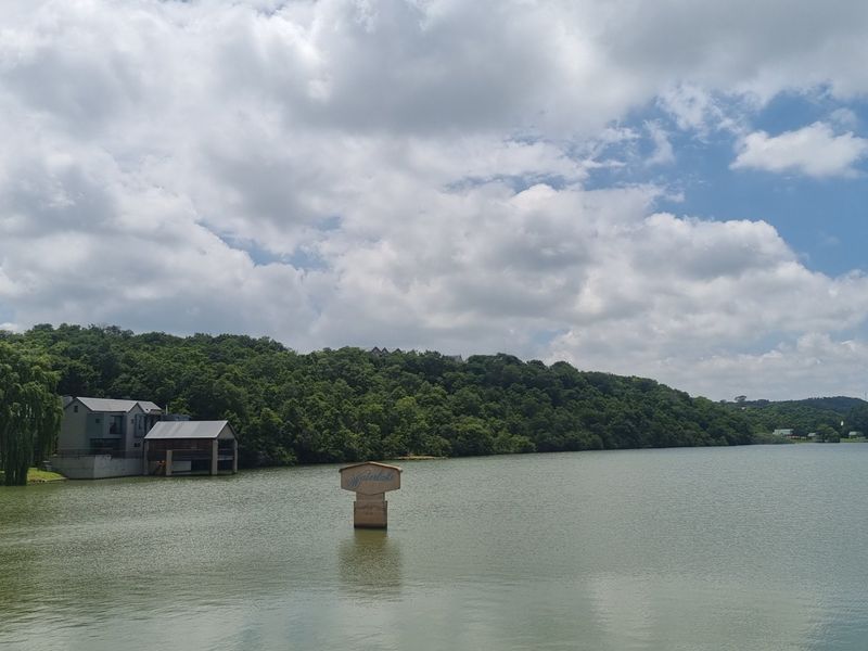 A scenic view of a large lake with a wooded hillside in the background and a small structure visible on the left bank.