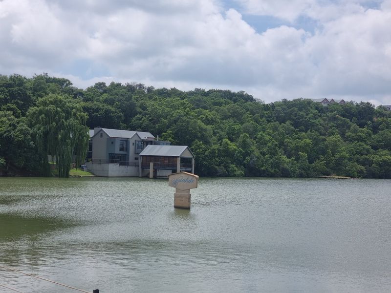 A scenic view of a lake featuring a waterfront residential property and a prominent estate sign.