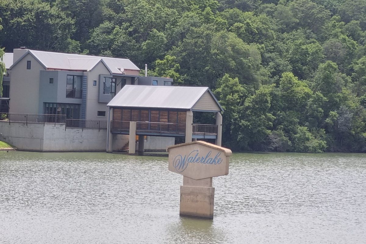 A scenic view of a waterfront property featuring a modern residence with a metal roof and a private deck extending over the lake.