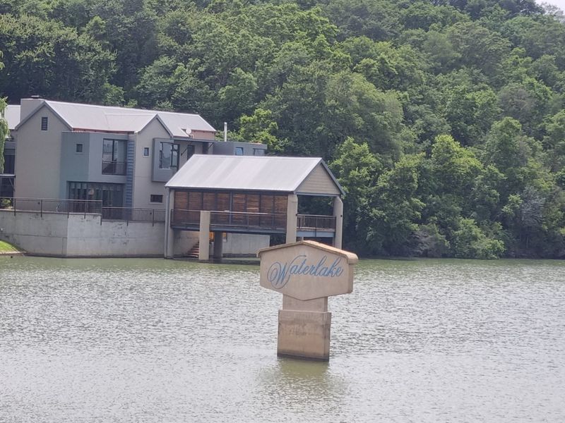 A scenic view of a waterfront property featuring a modern residence with a metal roof and a private deck extending over the lake.