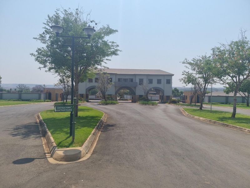 A well-maintained gated residential estate entrance featuring a paved driveway, landscaped verges, and a secure access gatehouse.