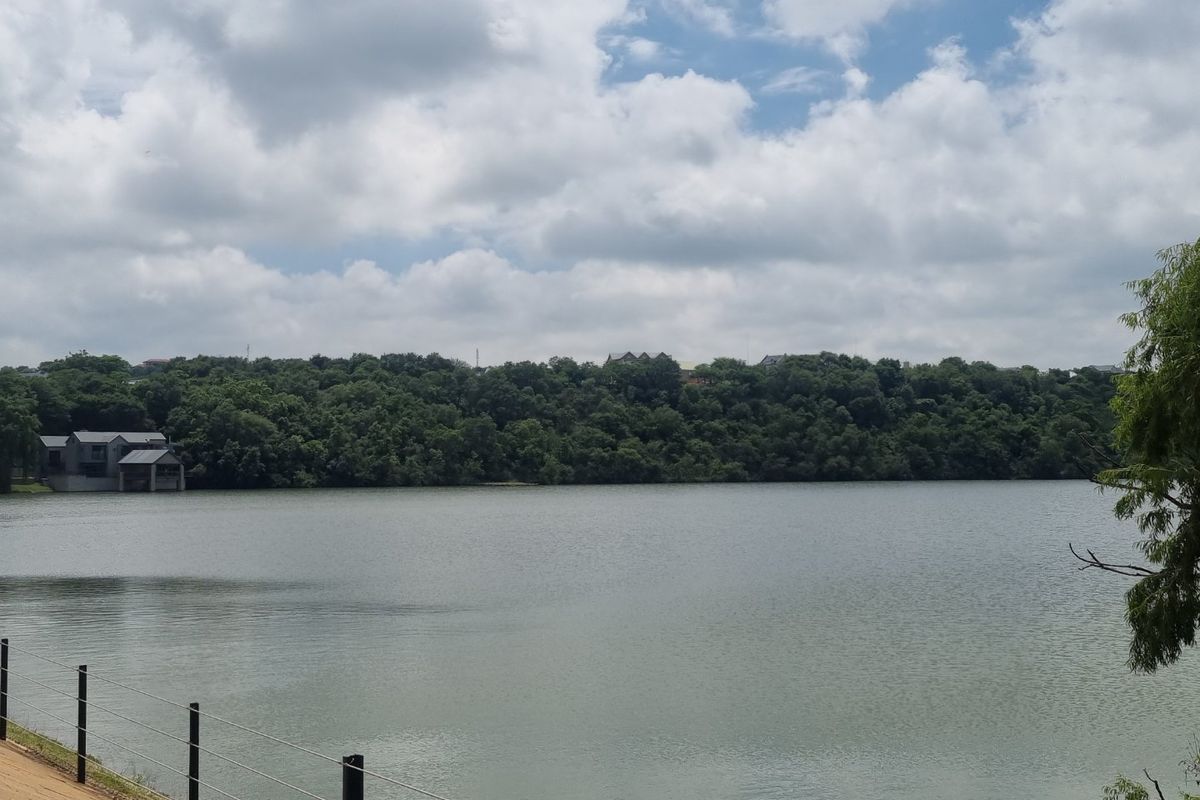 A scenic view of a large lake surrounded by dense trees and vegetation, featuring a wire fence in the foreground.