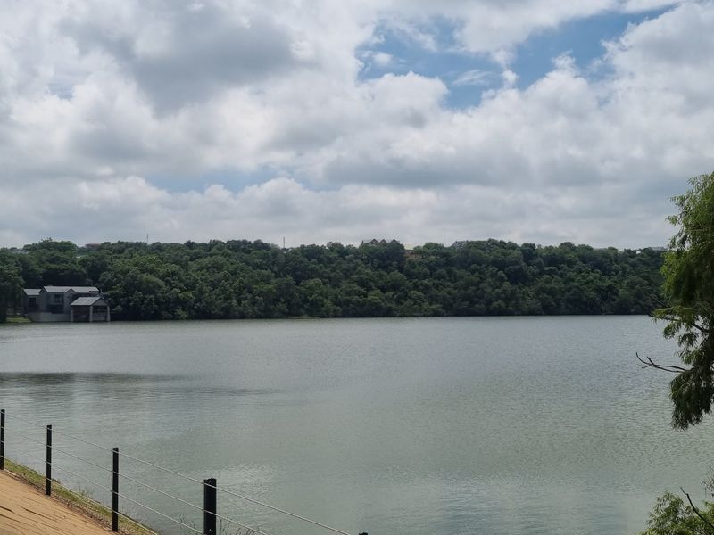 A scenic view of a large lake surrounded by dense trees and vegetation, featuring a wire fence in the foreground.