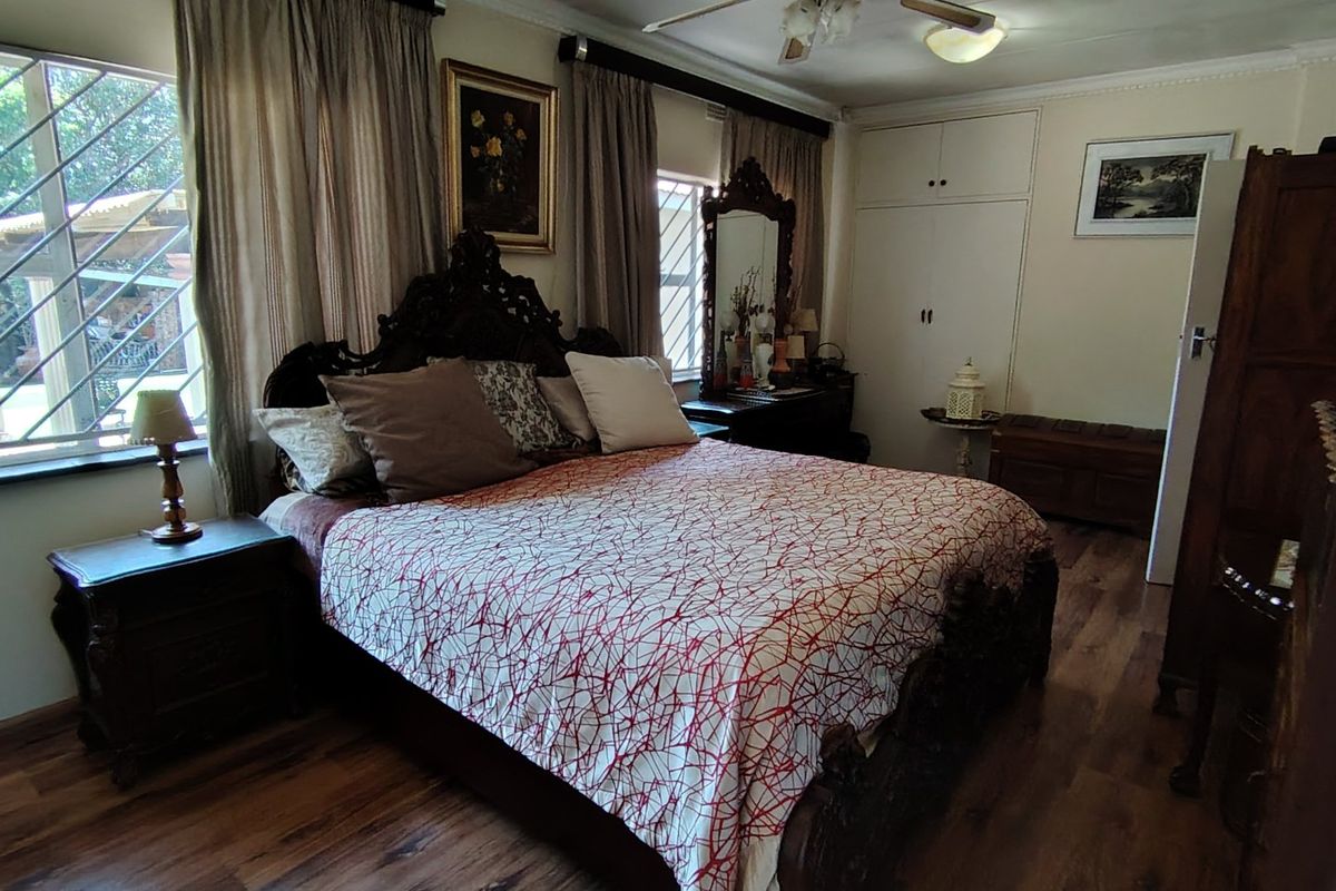 A bedroom featuring laminate flooring, built-in cupboards, and security bars on the windows, providing a functional and private sleeping space.