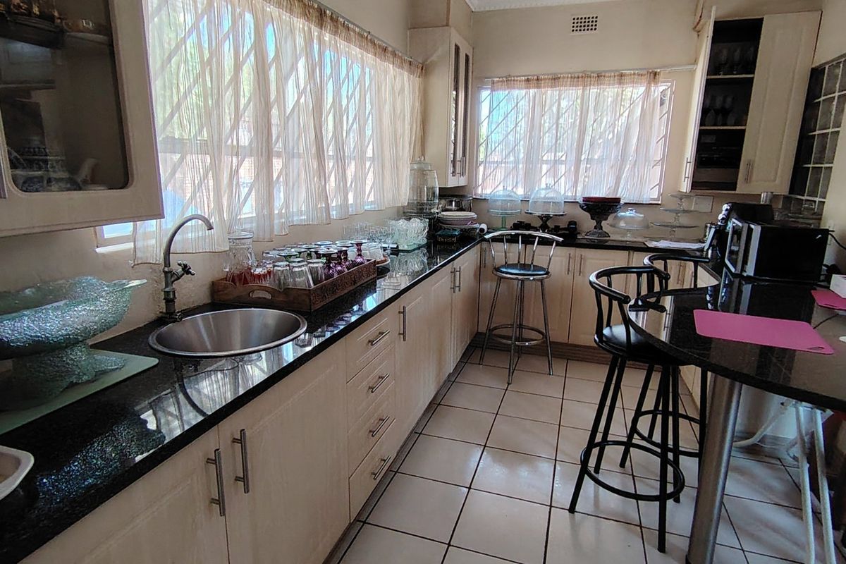 A functional kitchen featuring granite countertops, ample built-in cabinetry, a breakfast bar, and tiled flooring with large windows providing natural light.