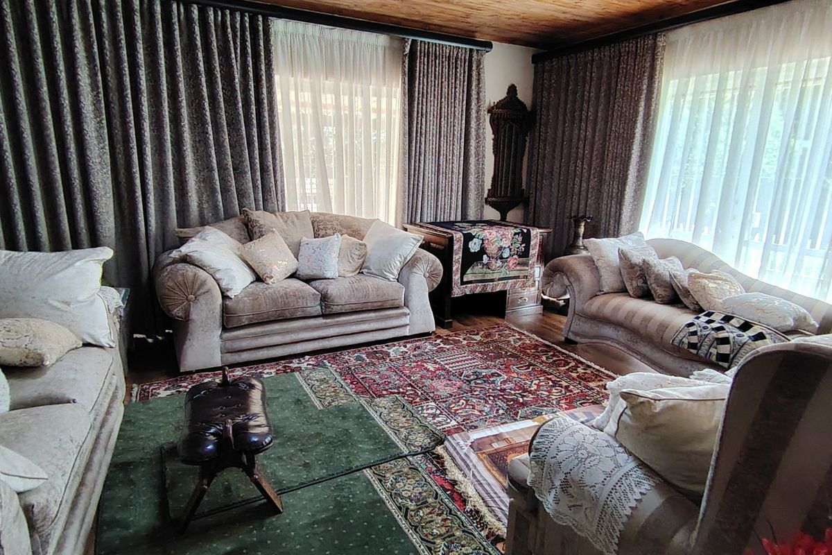 A spacious living room featuring a warm timber-paneled ceiling and large windows dressed with floor-to-ceiling curtains.