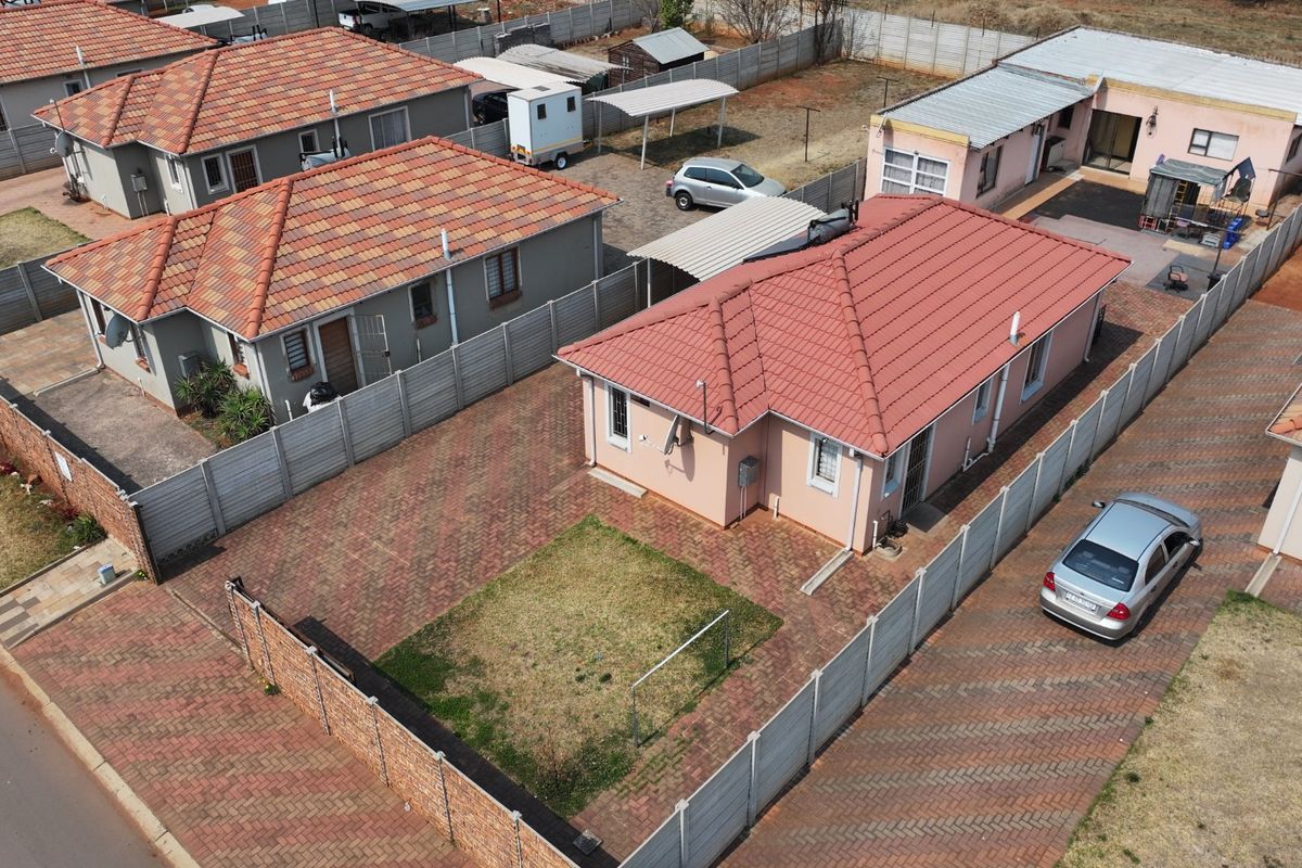 Aerial view of a residential property featuring a tiled roof house, paved driveway, and perimeter precast concrete walling within a suburban estate.