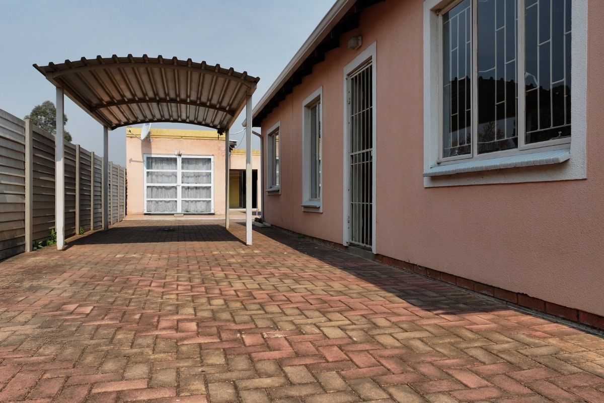 Rear exterior view featuring a paved driveway, a covered carport, and secure window bars on the side of the house.