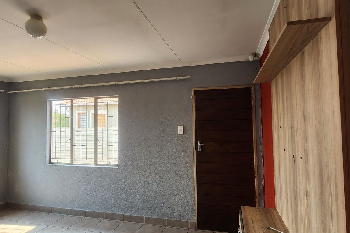 A living room featuring tiled flooring, a built-in wooden media unit, and security bars on the windows.