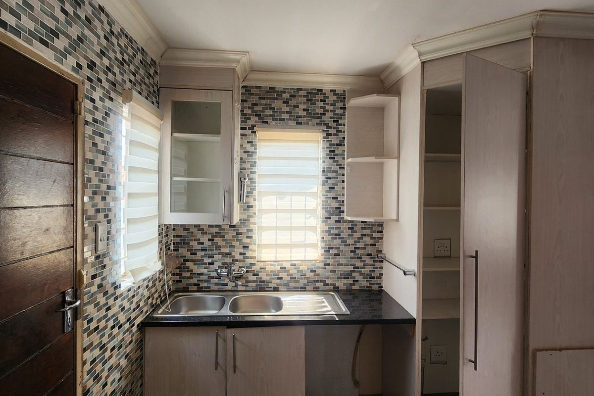 A compact kitchen featuring mosaic tile backsplashes, granite countertops, a double bowl sink, and built-in cabinetry with crown molding details.