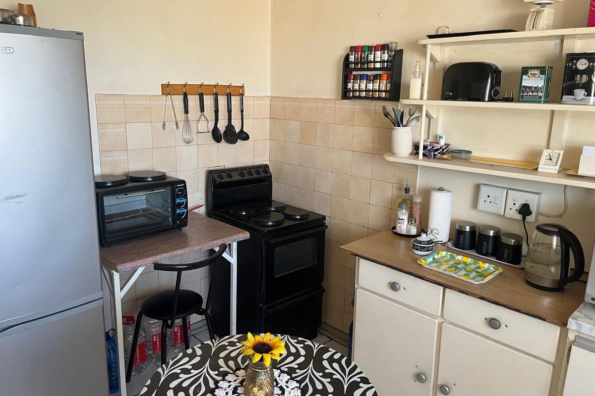 A compact kitchen featuring a tiled splashback, built-in cabinetry, and an electric stove, offering a functional layout with potential for cosmetic updates.
