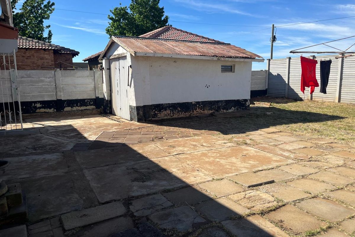 Rear exterior view showing a detached garage, paved patio area, and perimeter precast concrete walling.