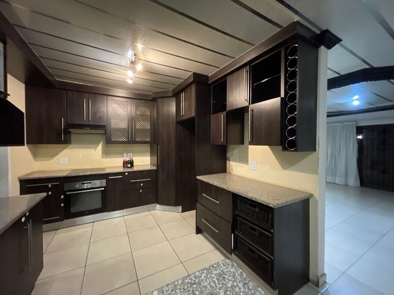 Modern kitchen featuring dark wood cabinetry, granite countertops, built-in oven, electric hob, and integrated wine storage with neutral tiled flooring.