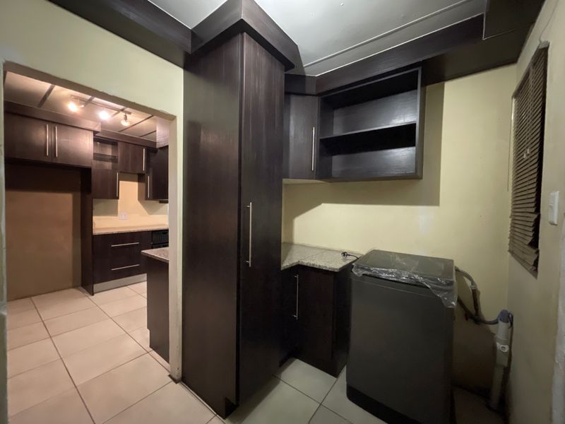 A functional scullery area featuring dark built-in cabinetry, granite countertops, and tiled flooring, with direct access to the adjacent kitchen space.