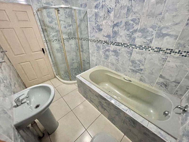 A functional bathroom featuring a pedestal basin, a separate shower enclosure, and a built-in bathtub with blue-toned marble-effect wall tiling.