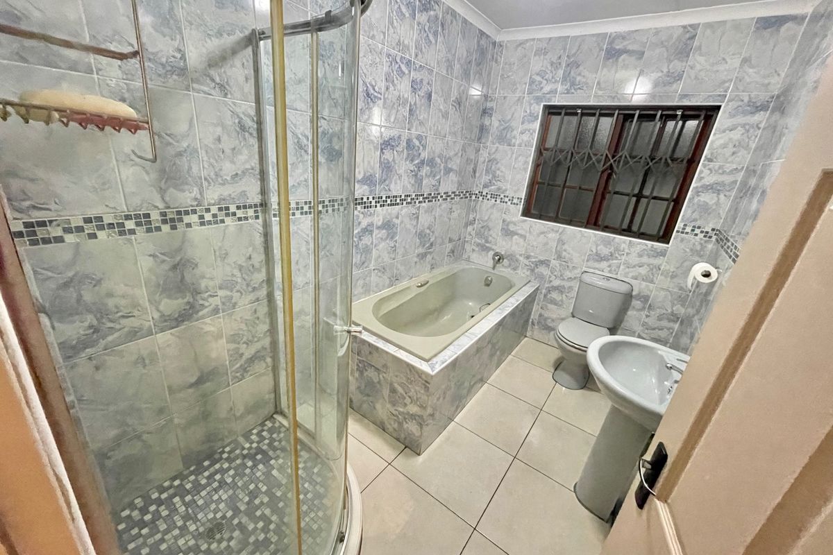 A functional bathroom featuring a shower enclosure, built-in bathtub, pedestal basin, and toilet, finished with blue marble-effect wall tiles and neutral floor tiles.