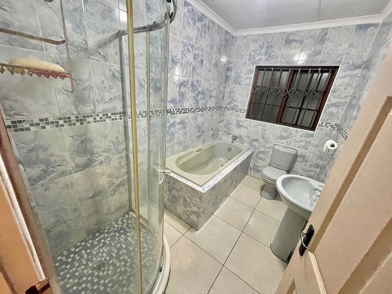 A functional bathroom featuring a shower enclosure, built-in bathtub, pedestal basin, and toilet, finished with blue marble-effect wall tiles and neutral floor tiles.