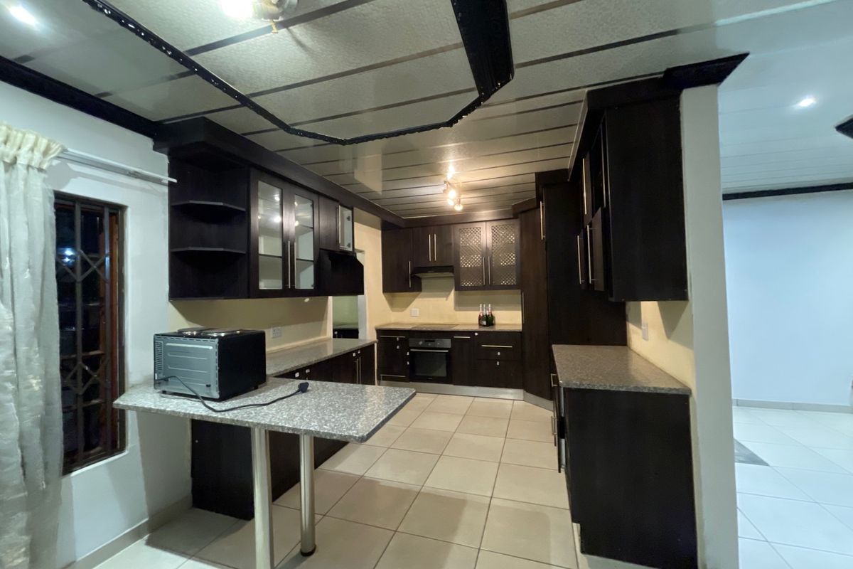 A functional kitchen featuring dark built-in cabinetry, granite countertops, a breakfast bar, and integrated appliances with neutral floor tiling.