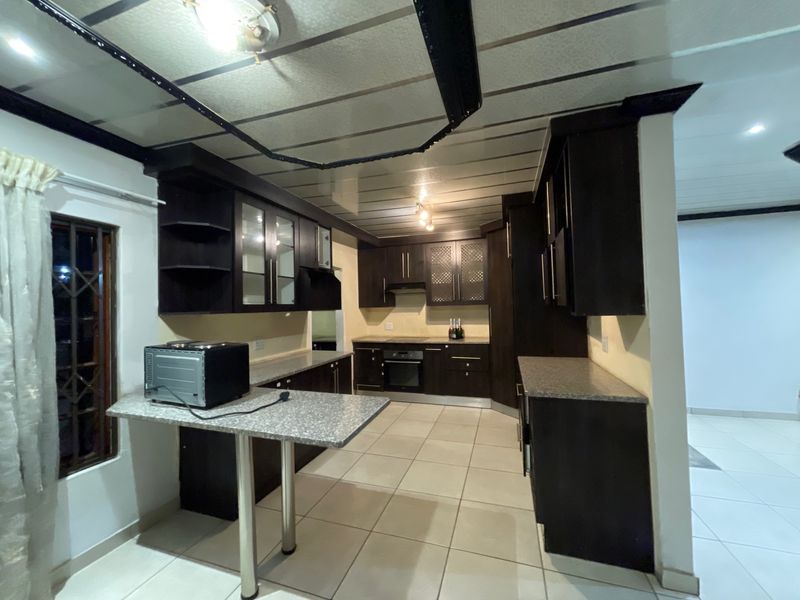 A functional kitchen featuring dark built-in cabinetry, granite countertops, a breakfast bar, and integrated appliances with neutral floor tiling.