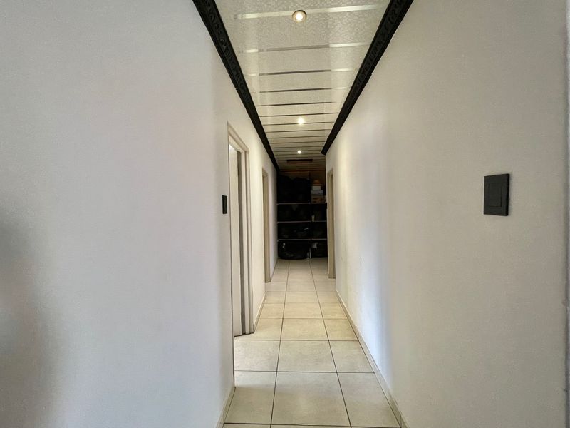 A clean, tiled hallway featuring recessed ceiling lighting and decorative trim, providing access to multiple rooms.